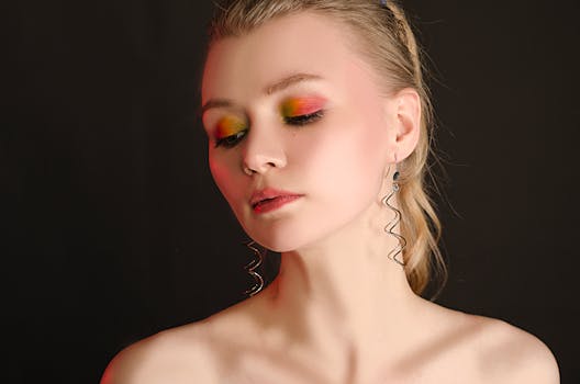 Portrait of a woman with vivid eye makeup, looking down gracefully against a dark backdrop.