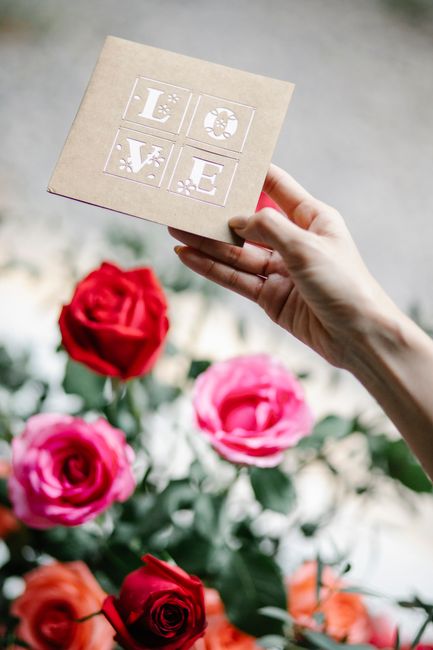 Crop anonymous female showing greeting card with Love title above blossoming rose bouquet during festive event