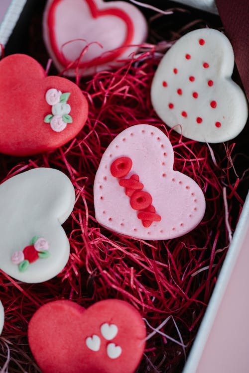 From above of colorful sweet cookies with glaze placed in box with red paper filling during Saint Valentines day celebration