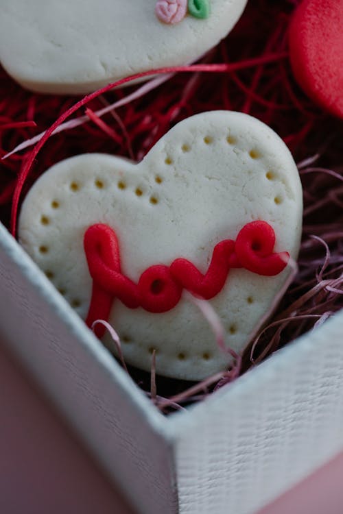 From above of tasty cookie with white frosting and romantic word in gift box decorated with paper filling during Saint Valentines day