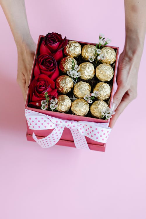 Free From above of anonymous female with gift box full of red roses and wrapped candies on red background during Saint Valentines day Stock Photo