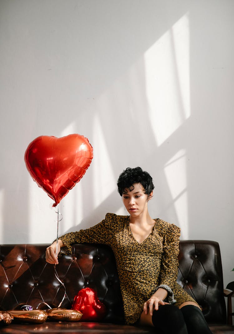 Pensive Woman With Red Balloon On Sofa During Holiday