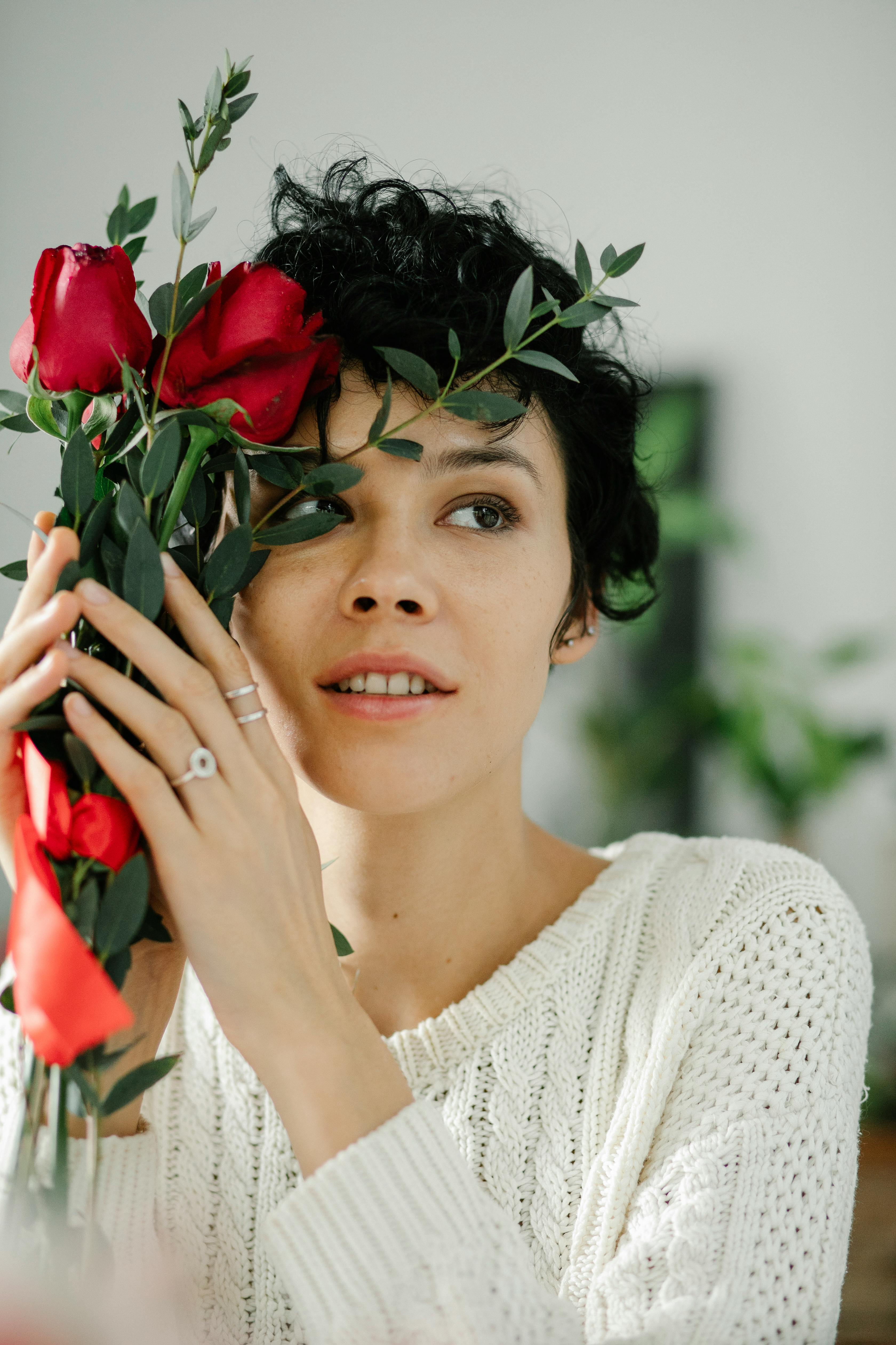 A woman holding red roses indoors, exuding elegance and warmth.