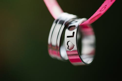 Soft focus macro of silver rings with engraved Love inscription and heart hanging on pink ribbon during romantic holiday celebration