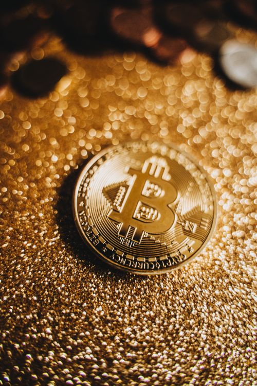 Free A macro shot of a bitcoin coin resting on a glittery gold surface, emphasizing wealth and digital currency. Stock Photo