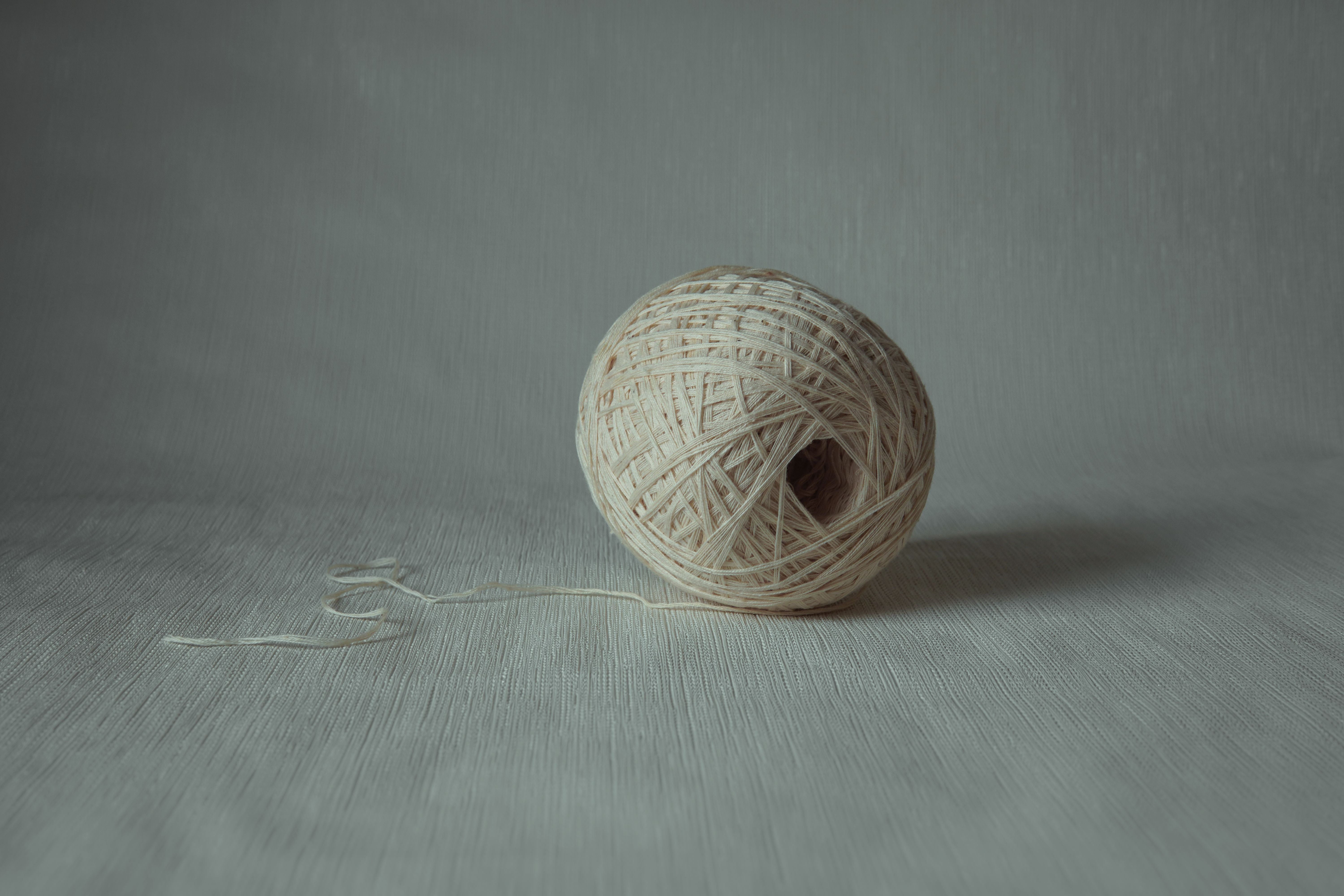 A simple ball of yarn resting on a textured surface in a minimalist setting.