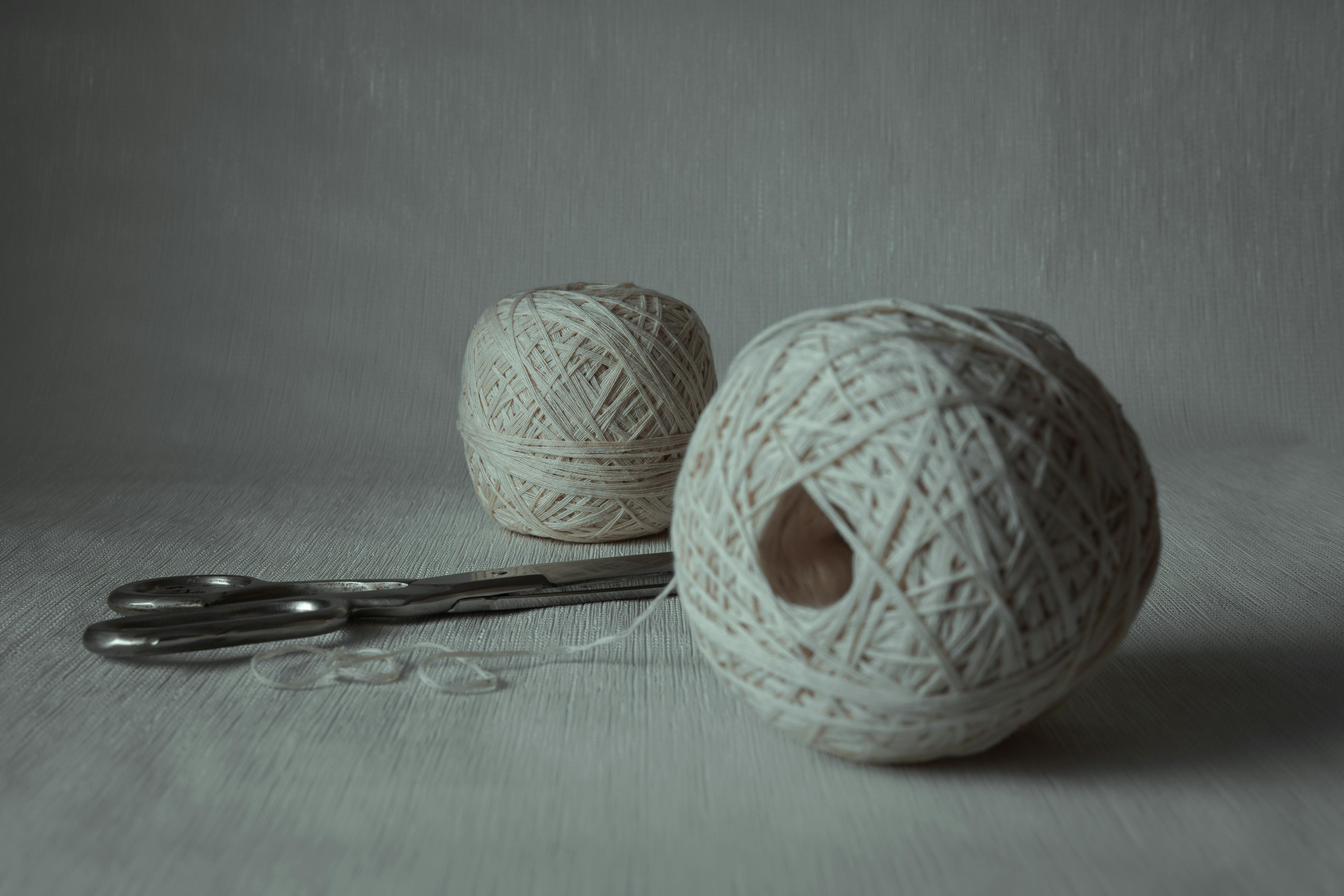 Close-up of yarn balls and scissors on a plain surface; minimalist design.