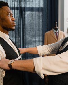 Professional tailor takes measurements for a bespoke suit fitting in a tailoring workshop.