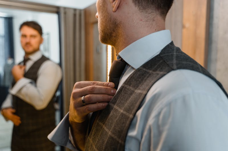 Man adjusting his tie in front of a mirror, getting ready