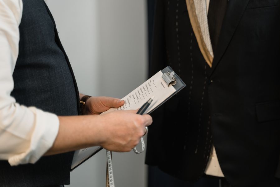 Tailor taking measurements and notes with a clipboard and tape measure in a fashion studio