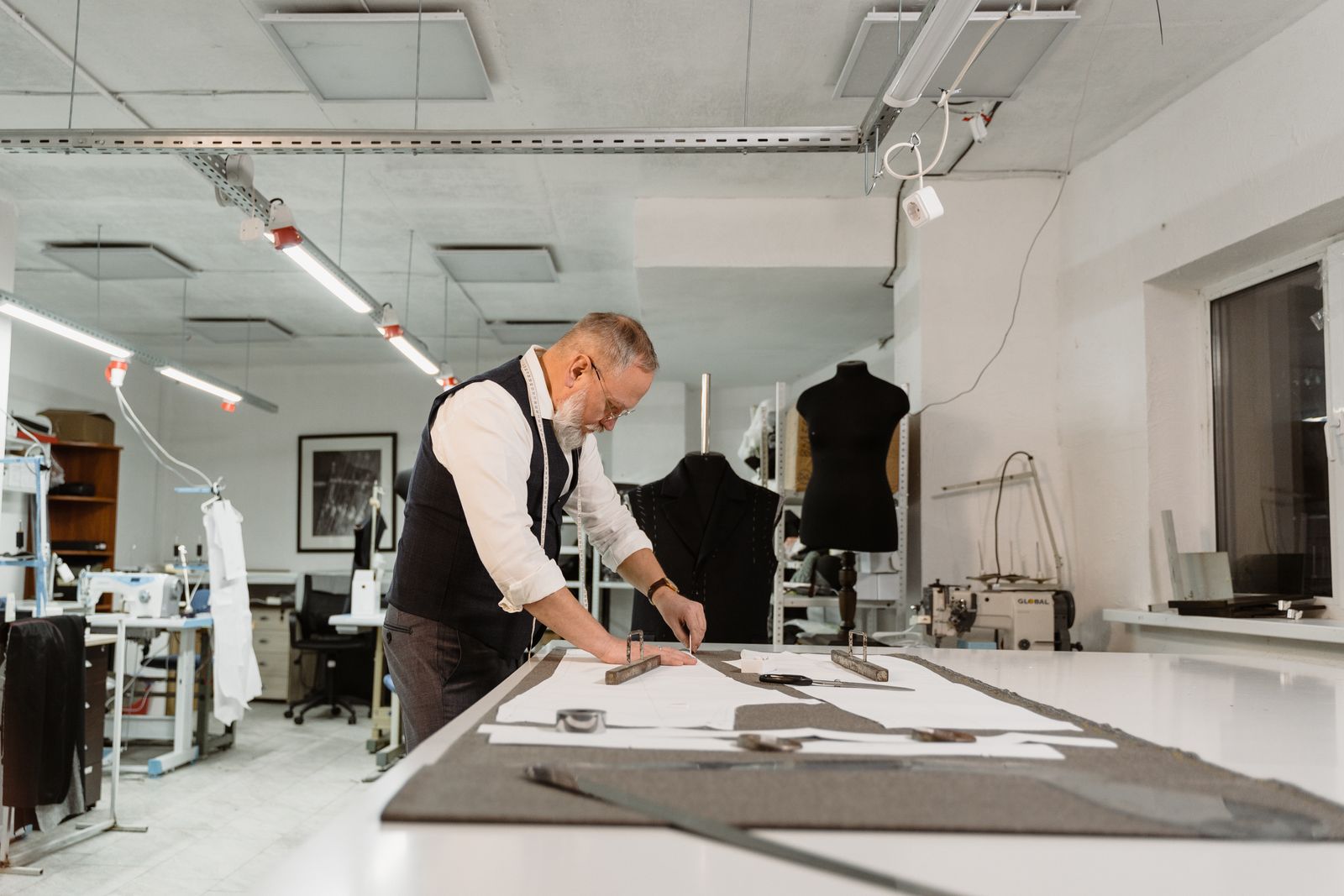 A tailor chalking a line across grey cloth on a cutting table