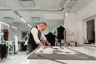 Male tailor meticulously crafting garment patterns at worktable in studio.
