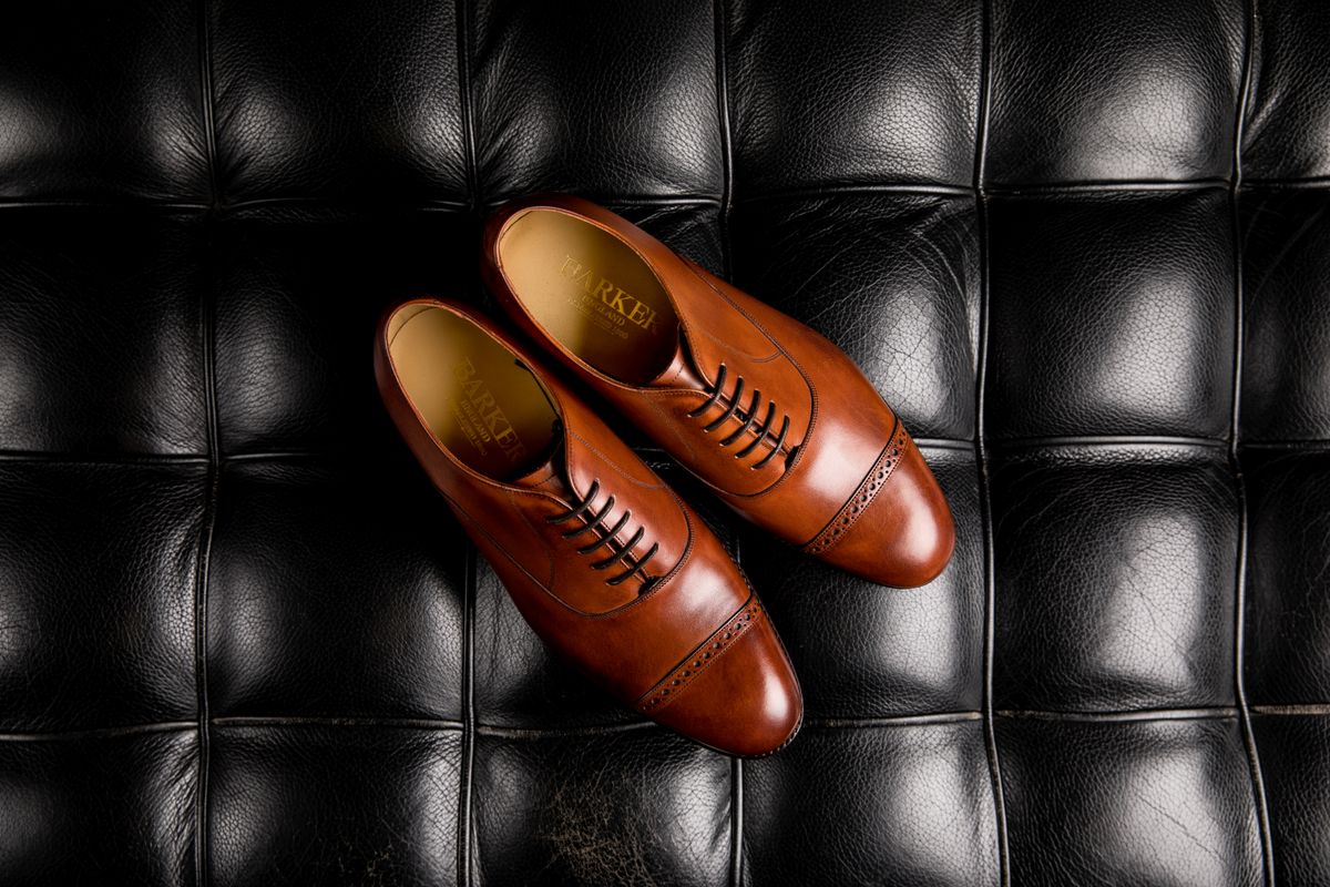 Par de sapatos oxford masculinos em couro marrom sobre superfície escura, calçado clássico