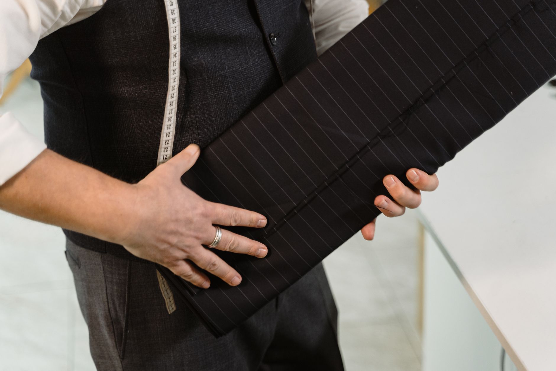 Tailor holding roll of pinstriped fabric in a workshop setting.