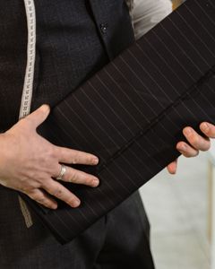 Tailor holding roll of pinstriped fabric in a workshop setting.