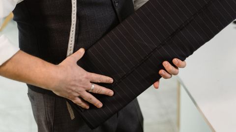 Tailor holding roll of pinstriped fabric in a workshop setting.