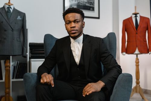 Free A stylish man in a tailored suit seated inside a fashion showroom, exuding elegance. Stock Photo