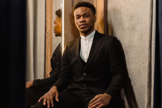 Man in a Black Suit Sitting Beside a Mirror