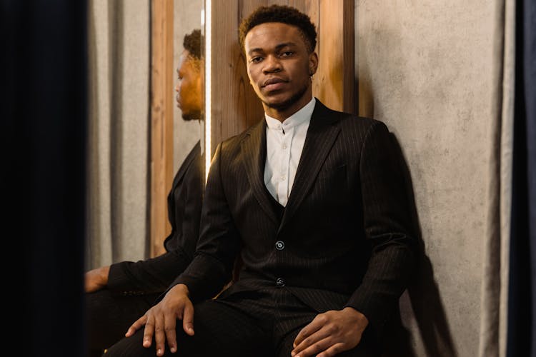 Man In A Black Suit Sitting Beside A Mirror