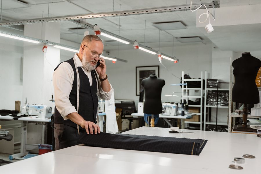 Professional tailor in workshop taking a phone call, working on fabric with sewing tools.