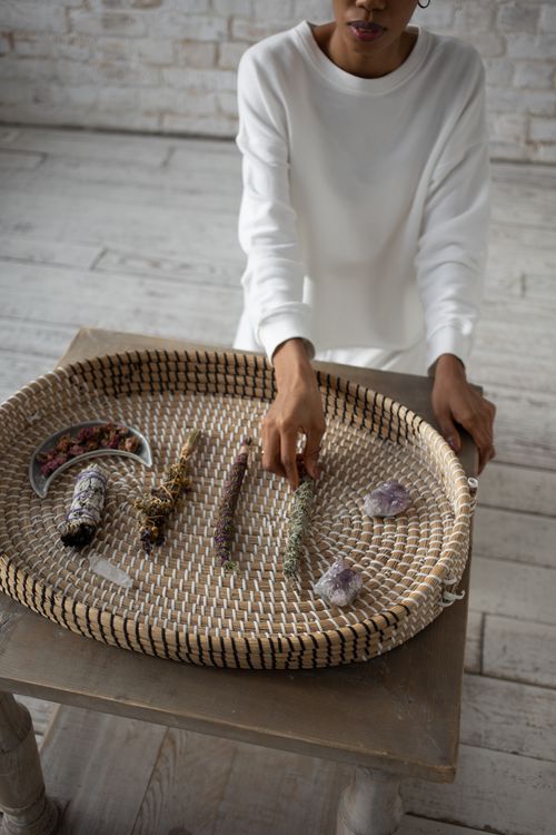 Free Woman organizing crystals and dried herbs on a large woven basket indoors, showcasing holistic and spiritual practices. Stock Photo