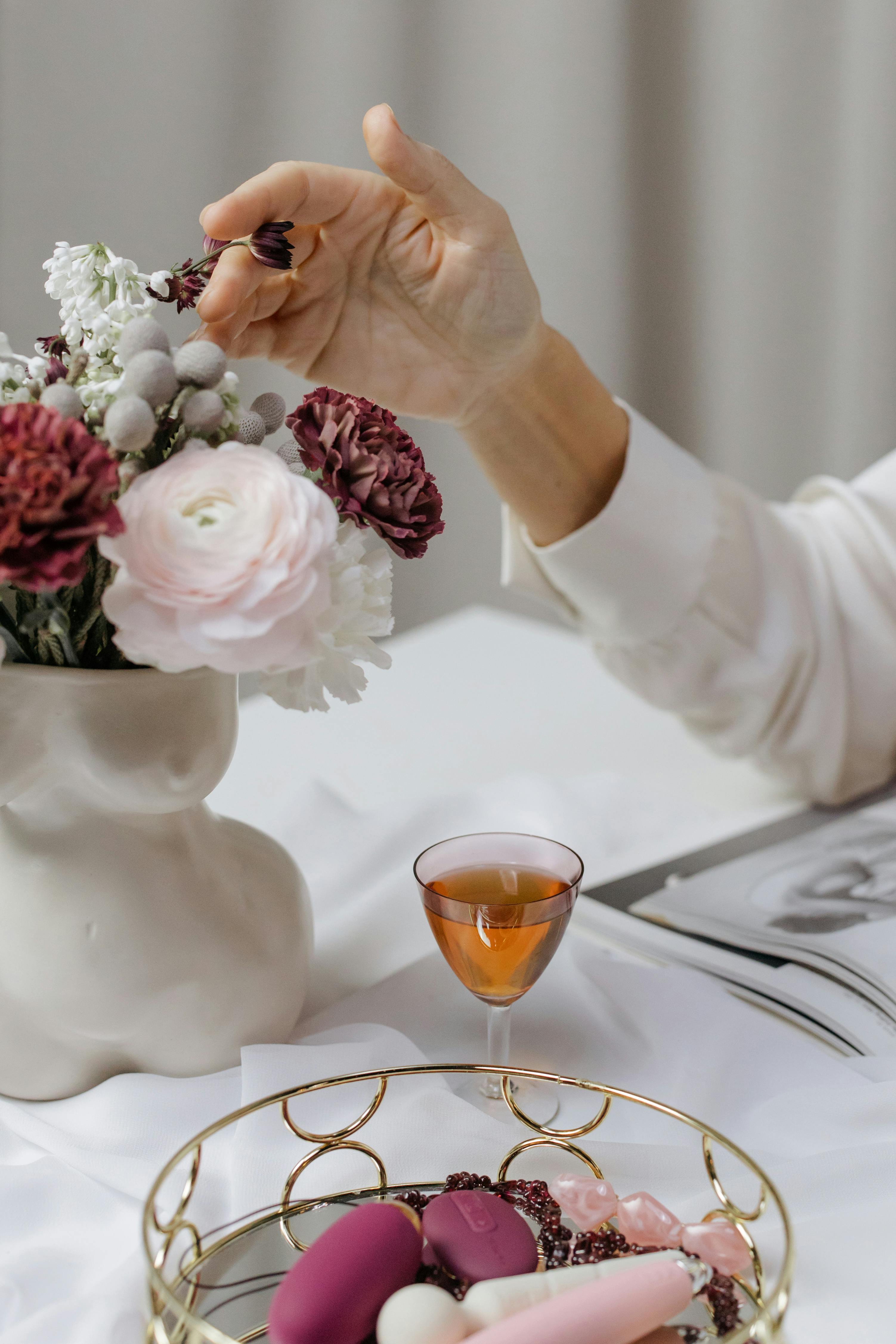 woman in white long sleeve shirt holding red flower on white ceramic vase