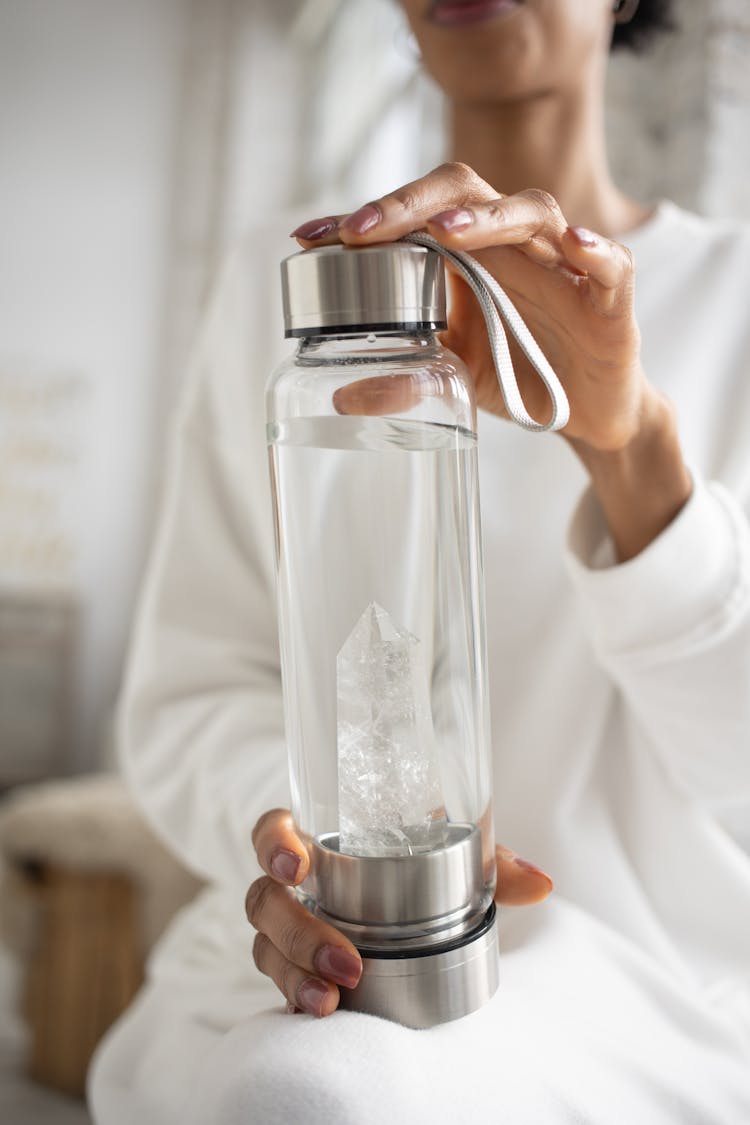 Close-up Of A Woman Holding A Water Bottle With A Crystal Inside 