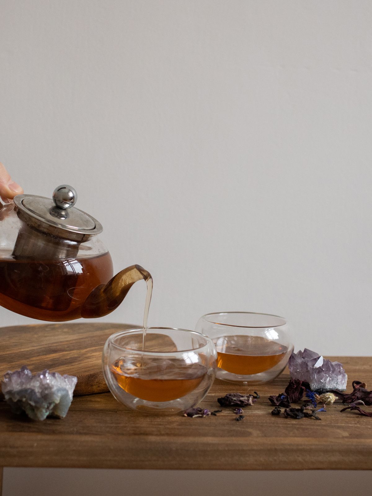 手持玻璃茶壺將熱茶倒入茶杯,木托盤上擺放紫水晶原礦