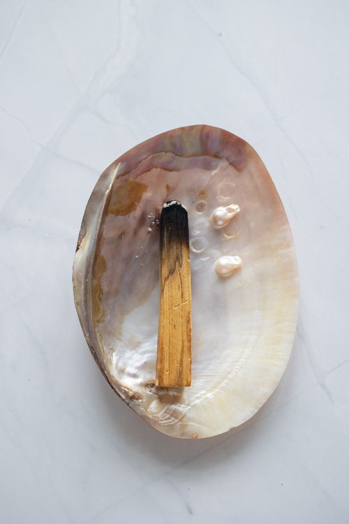 Free A piece of burnt palo santo wood rests on an ornate shell on a marble surface. Stock Photo