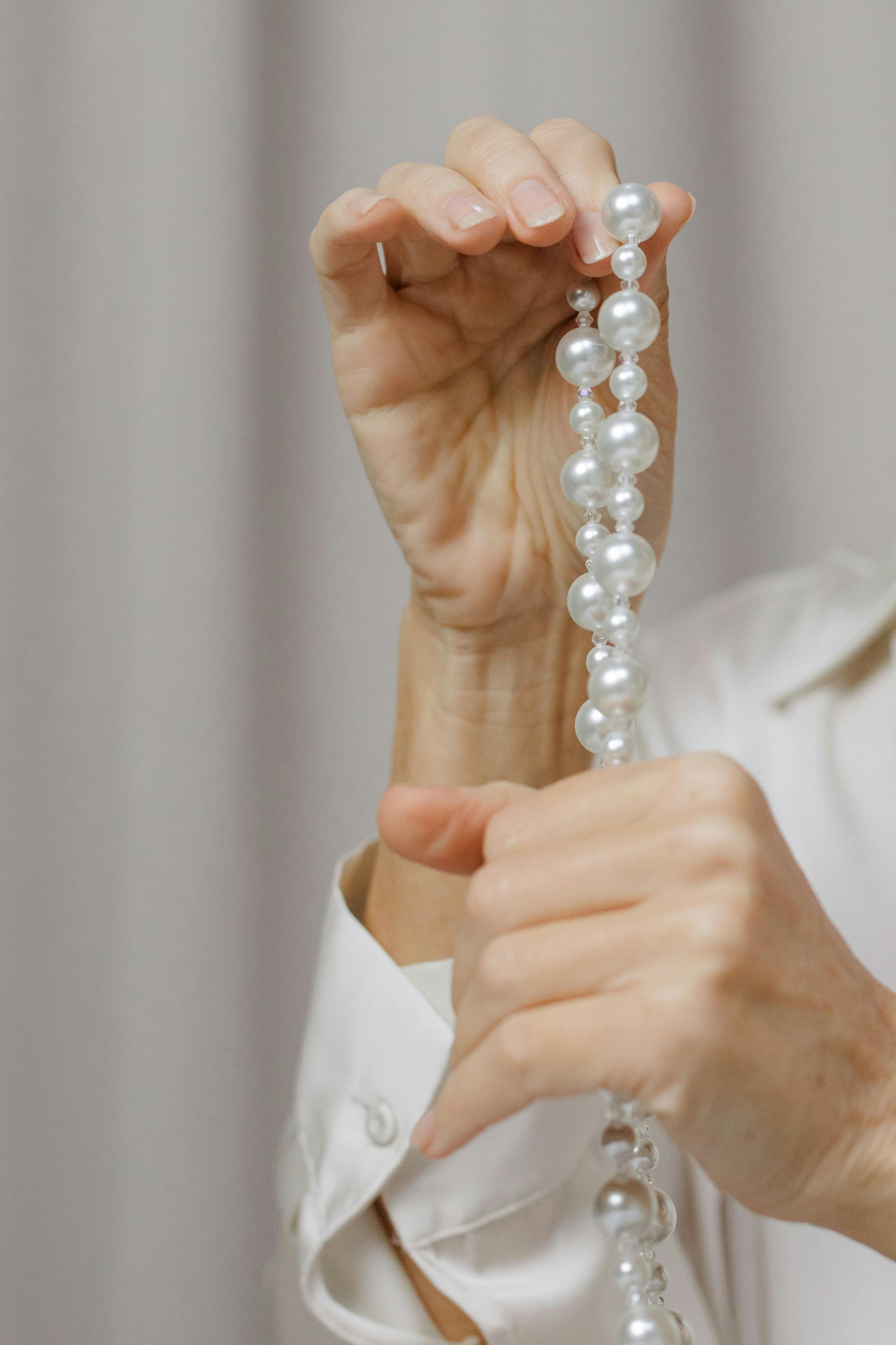 Close-up of hands gently holding a strand of elegant pearls, highlighting their texture.
