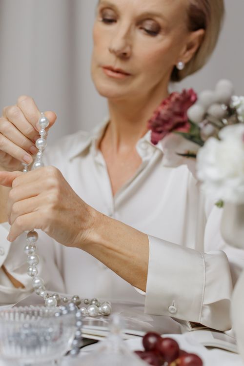 Free Sophisticated mature woman examining pearl necklace at an elegant table setting. Stock Photo