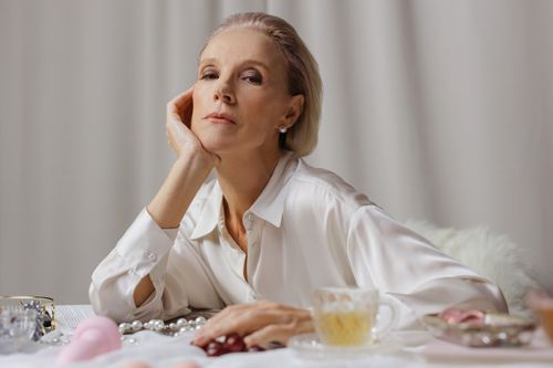 Free A poised senior woman in a white shirt enjoying tea, surrounded by elegant pearls. Stock Photo