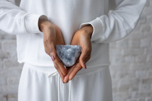 A close-up image of hands gently holding a celestine crystal against a textured background.