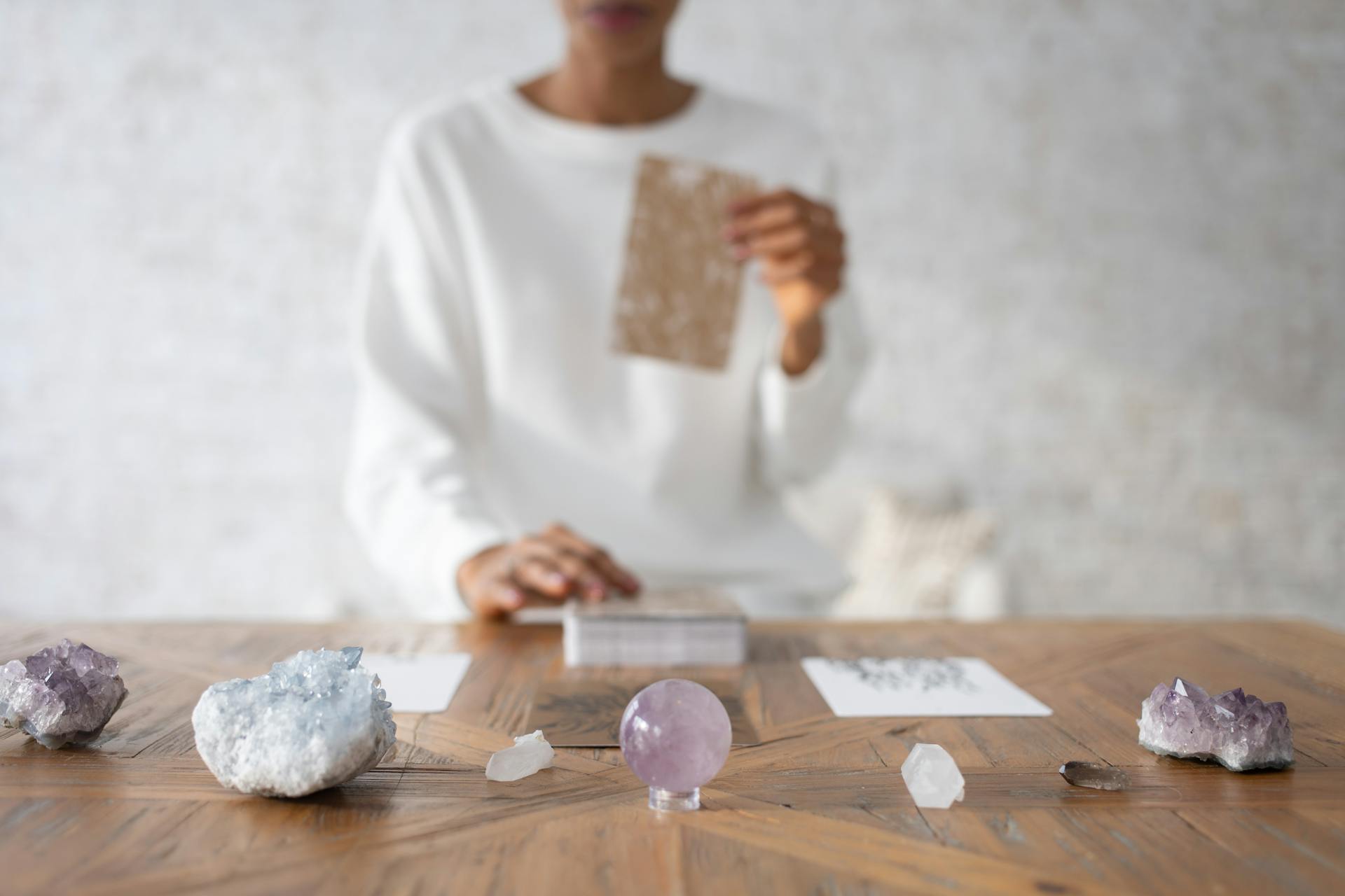 A person in focus arranging crystals and cards on a wooden table indoors.