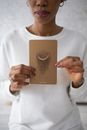 A Woman in White Sweater Holding a Card with Moon Drawing