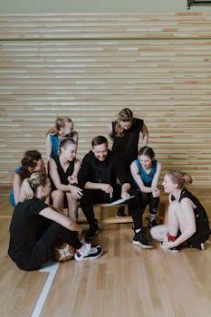 Basketball team and coach discuss strategies during training in a gymnasium.