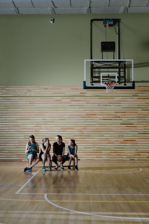 Free Group of young female basketball players sitting on a bench in an indoor court. Stock Photo