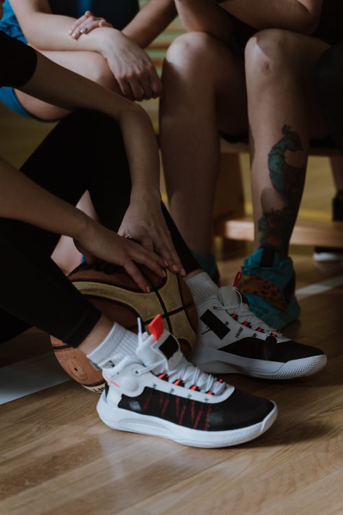 Free Close-up of casual basketball players sitting with sneakers and ball indoors. Stock Photo