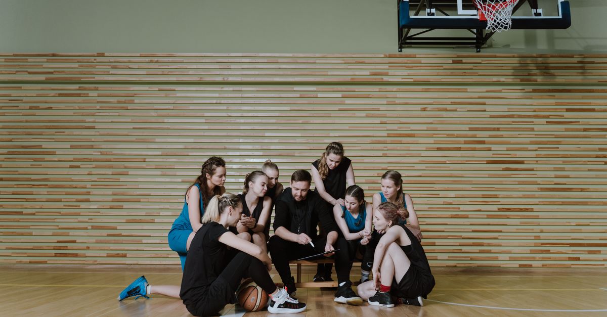 basketball team huddling with heads bowed, coach standing with them