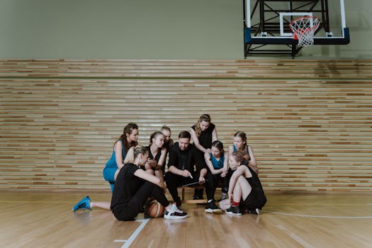 A coach discussing strategies with a female basketball team indoors on a court.