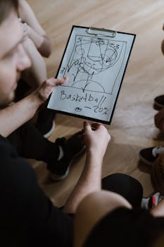 Coach presents a basketball strategy on clipboard during indoor team huddle.