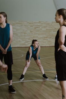 Group of female athletes stretching on an indoor basketball court preparing for training.