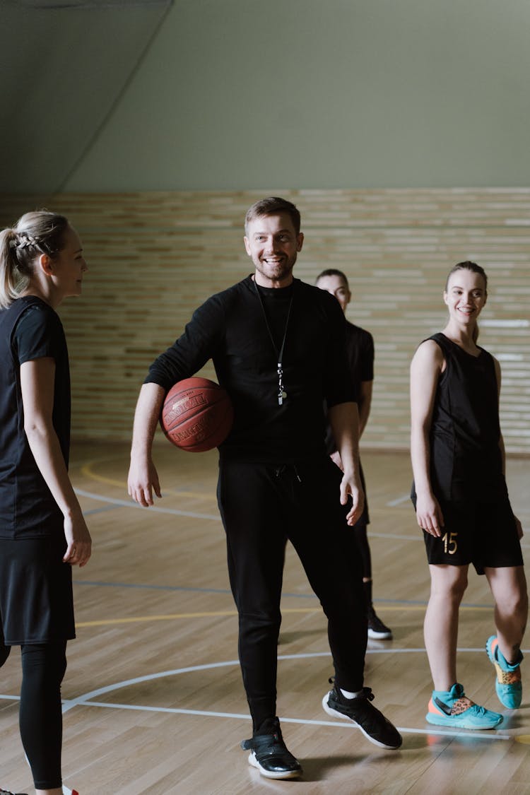 A Coach Holding The Ball While Talking To The Basketball Players