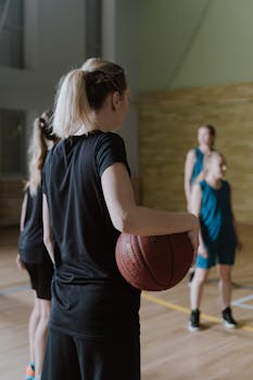 Back view of women athletes playing basketball indoors.