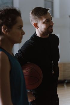 A basketball coach holding a ball while instructing a young player indoors.