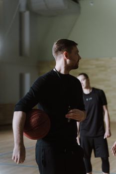 A basketball trainer holding a ball while guiding players in an indoor gym setting.