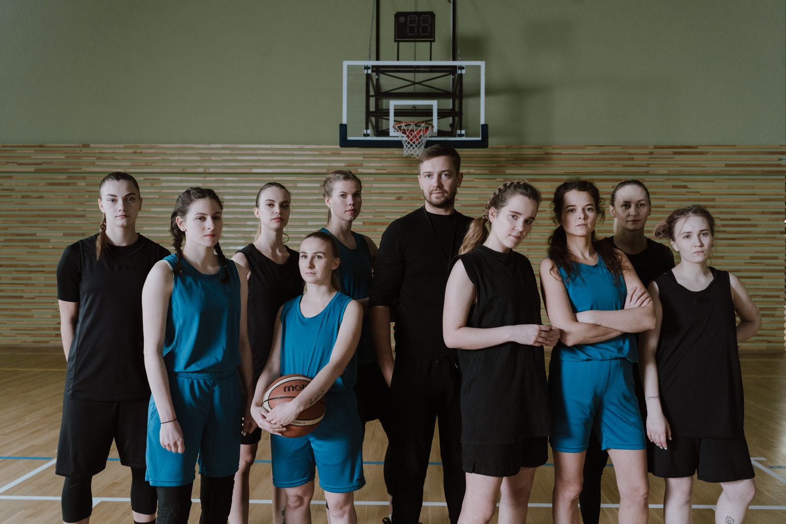 A women's basketball team poses together with their coach inside the gymnasium, representing the full roster.