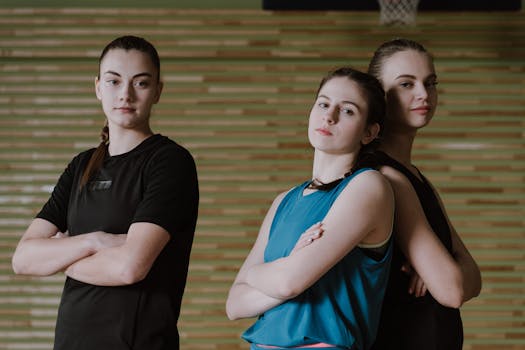 Three confident teenage girls in sports attire posing on an indoor basketball court.