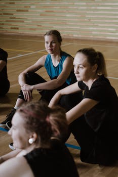 Young women basketball team members sitting and resting in an indoor gym.