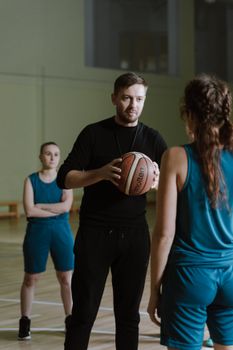 Indoor basketball training session with a coach instructing female players.
